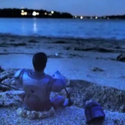 Armored space soldier on the beach at night with helmet beside him facing the waves