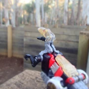 A robotic velociraptor perches on a wooden wall looking out into a giant wooden maze.