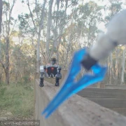 An action shot of a white-armored space arm holding an energy sword with a robotic velociraptor approaching menacingly, posed on a wood fence in a forest.