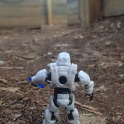 A white-armor space soldier in a wide wooden maze space with dirt floor, expectantly holding a blue energy sword.