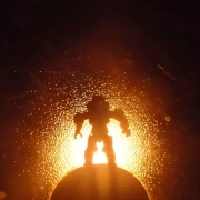 Silhouette of an armored space soldier standing atop a sphere with radiant yellow light glowing behind it them.