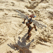 High angle view of a brown Bionicle with robotic wings walking on the beach in the middle of a human flip-flop footprint.
