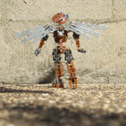 A brown Bionicle with robotic wings steps towards a brick wall while looking far upwards.