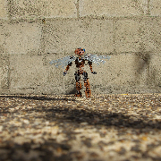 Wide shot of a brown Bionicle with robotic wings steps towards a brick wall while looking far upwards.